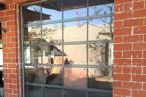 Industrial-style glass garage door with dark frames, set within a rustic red brick wall