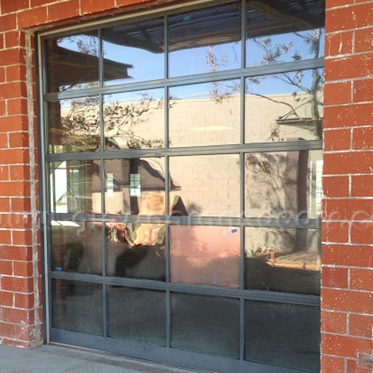 Industrial-style glass garage door with dark frames, set within a rustic red brick wall