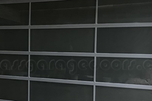 modern bp glass garage door with dark glass panels and sleek gray aluminum frames, providing privacy and a sophisticated look for a contemporary home or commercial building with stone cladding.